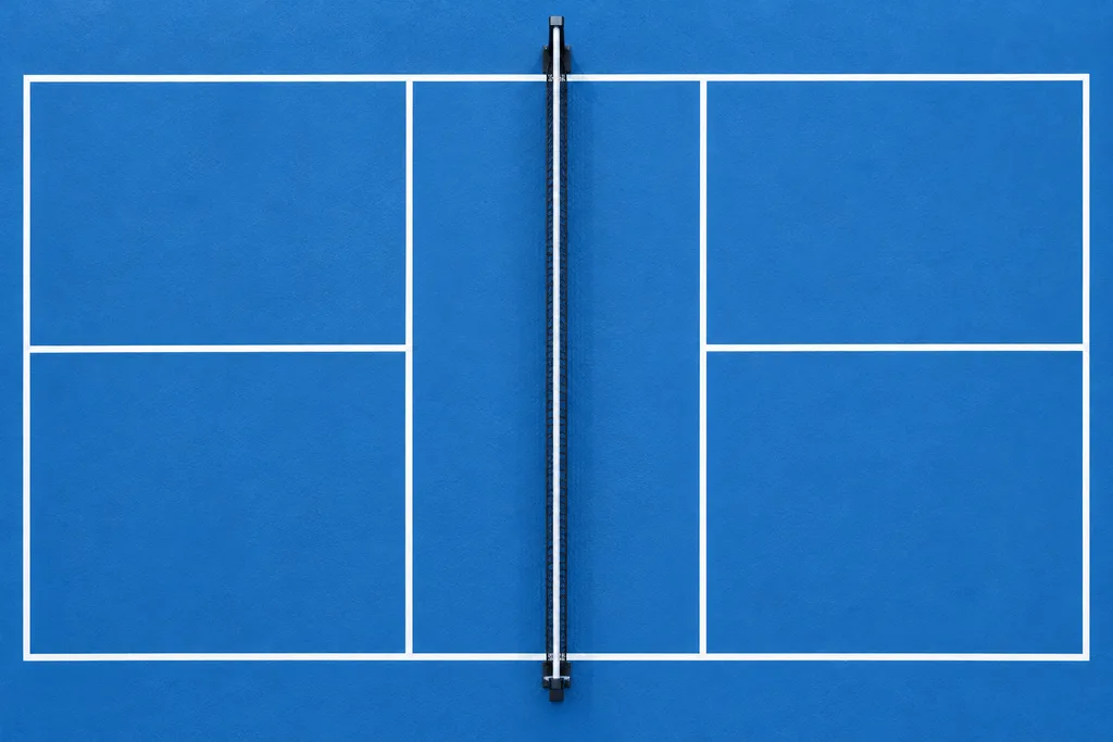 Vue de dessus d'un court de pickleball dessiné au sol, avec ses lignes blanches et le filet central.